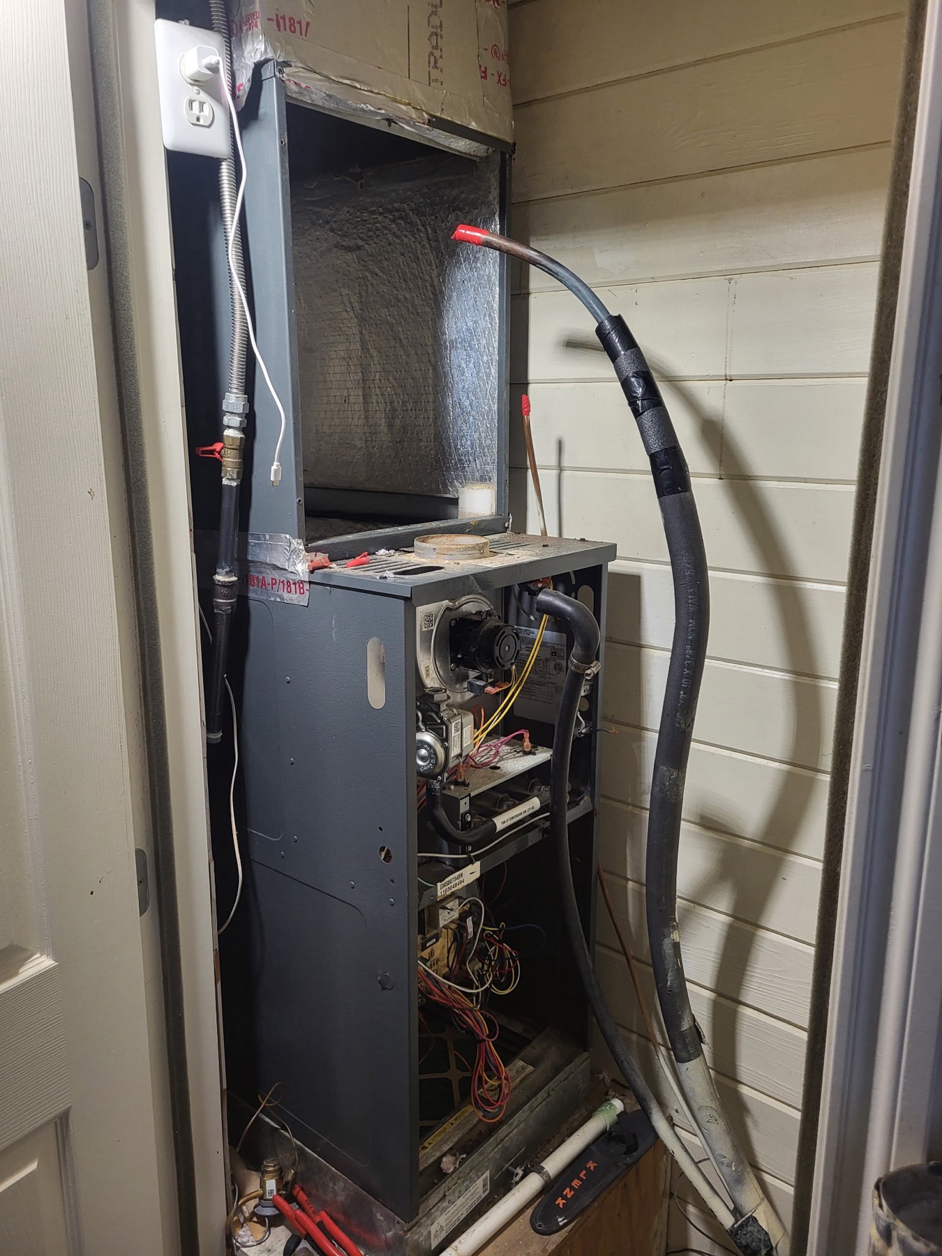 Furnace cabinet open in a hallway closet with the burners and control wiring exposed during a changeout