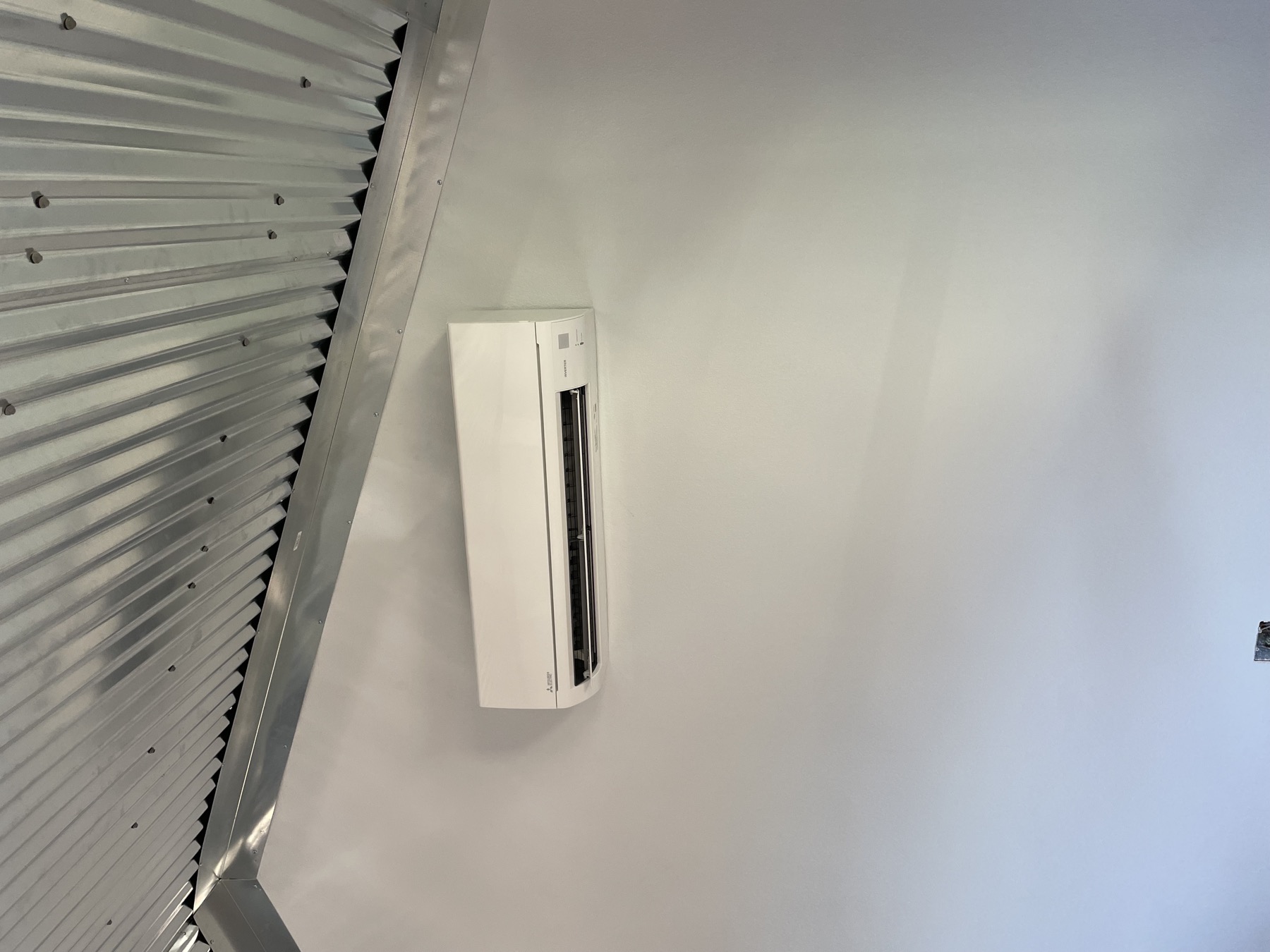 Mitsubishi mini split wall head mounted high under a corrugated metal ceiling
