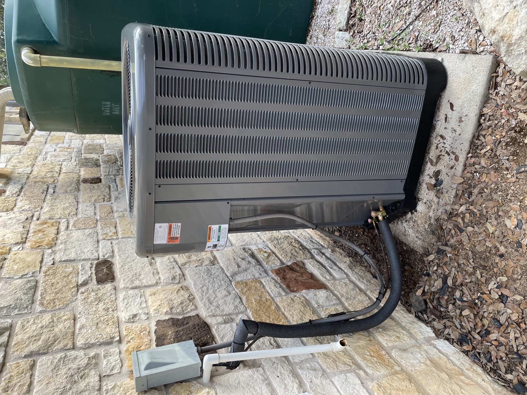 New Rheem condenser on a concrete pad against a stone wall, line set and condensate line run neatly to it