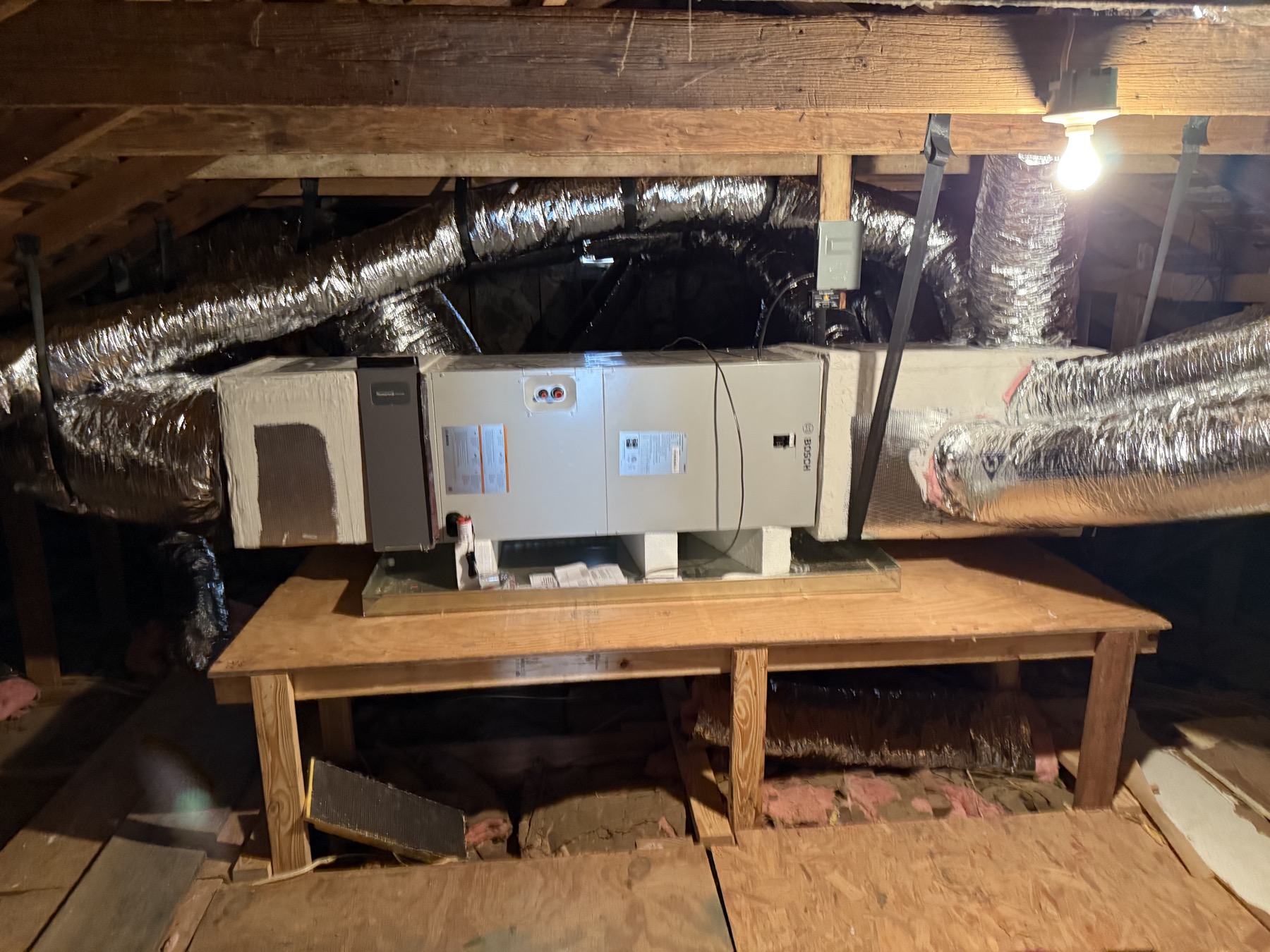 Bosch air handler on a wooden attic platform with insulated flex ducts leaving both ends