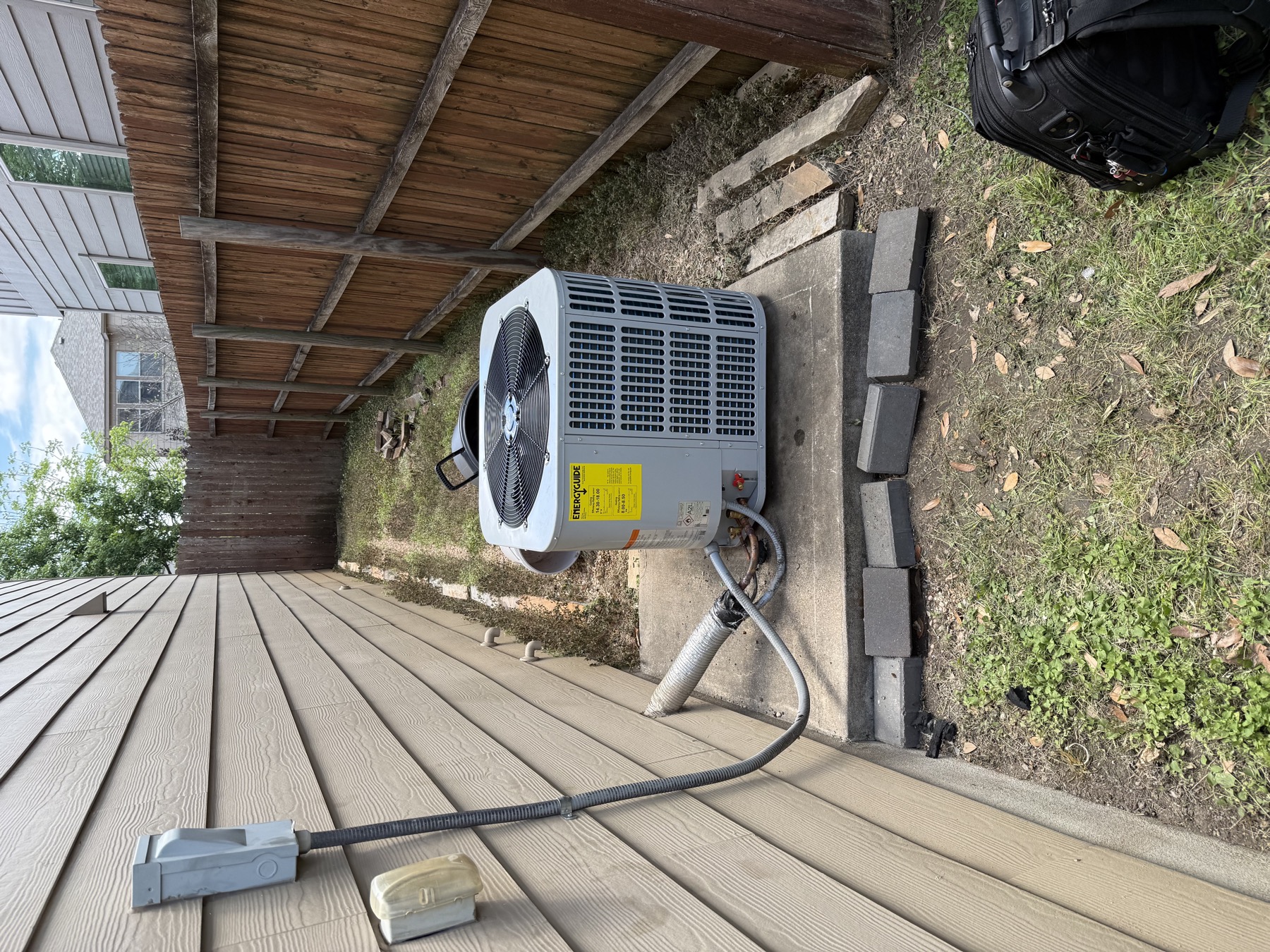 New condenser with its EnergyGuide label still on, set on a pad in a narrow side yard beside a privacy fence