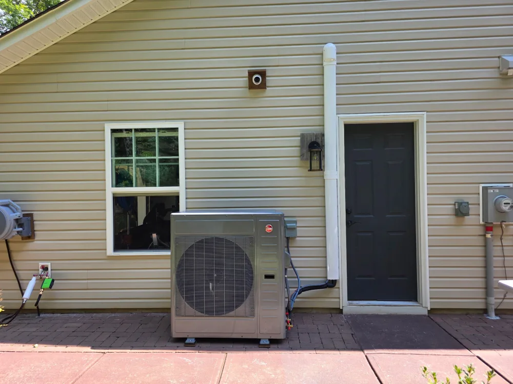 New Rheem outdoor unit set level on a paver patio with the line set sleeved and routed up the wall